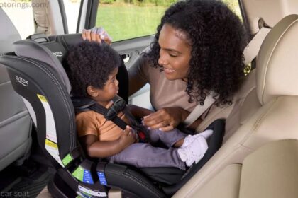 Smiling Canadian parent securely fastening a rear facing car seat with an infant inside a vehicle.